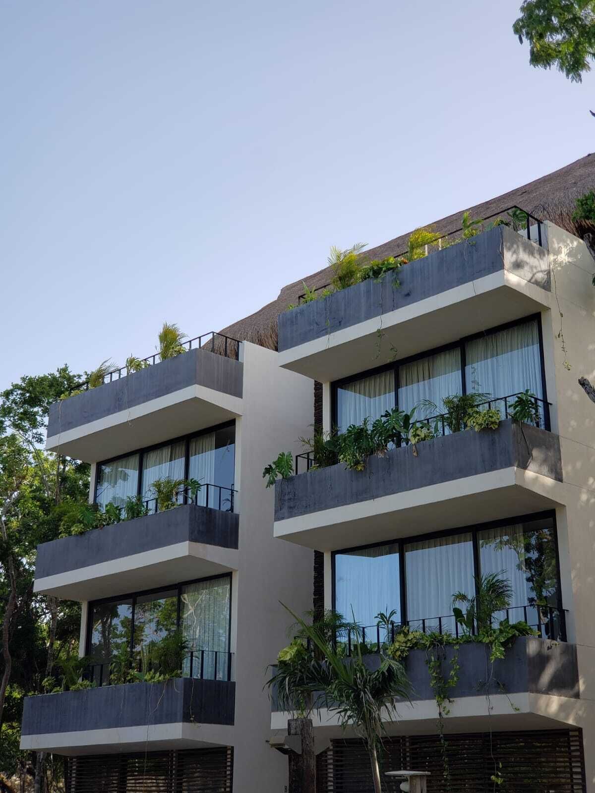 Un immeuble moderne à plusieurs étages, doté de balcons, de grandes fenêtres et de verdure.