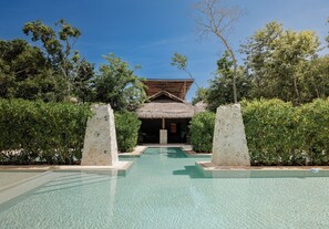 A swimming pool with a thatched-roof structure in the background. - BT Homes - Zama Luxury (Tulum)