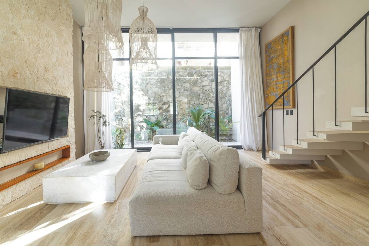 A modern living room with a large TV, a sofa, a coffee table, and a staircase.