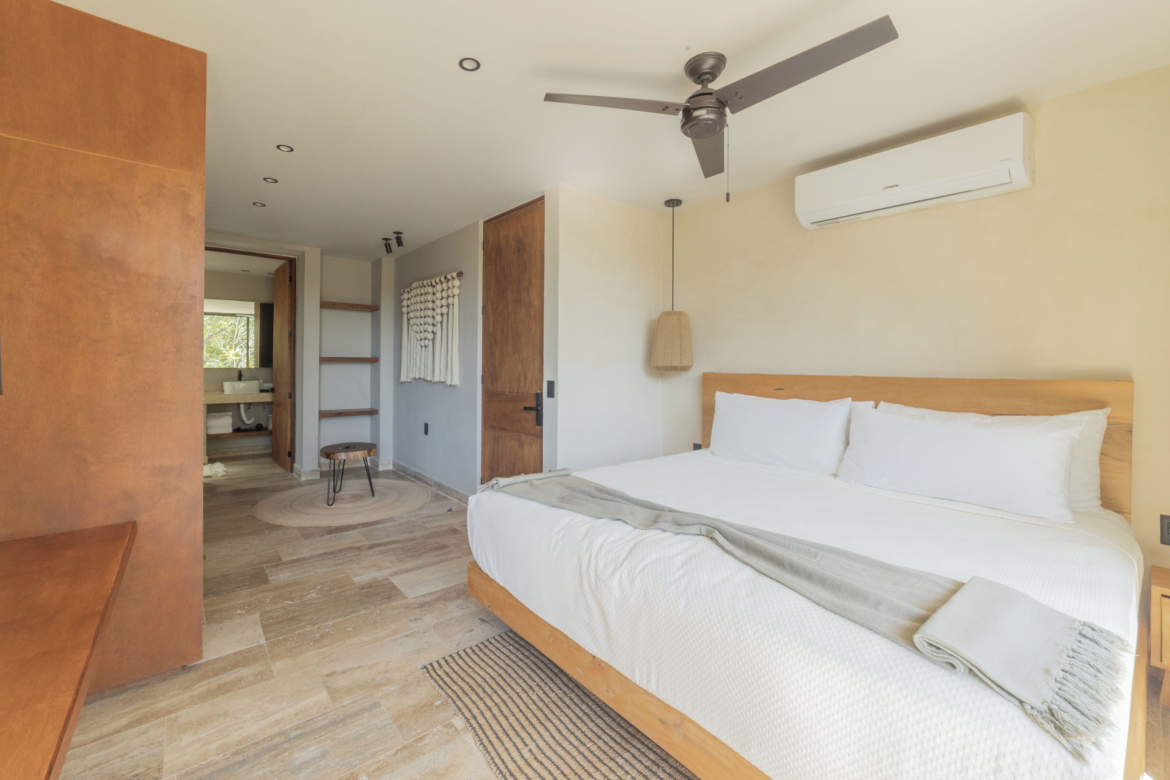 A modern bedroom with a large bed, wooden headboard, ceiling fan, and an air conditioning unit.