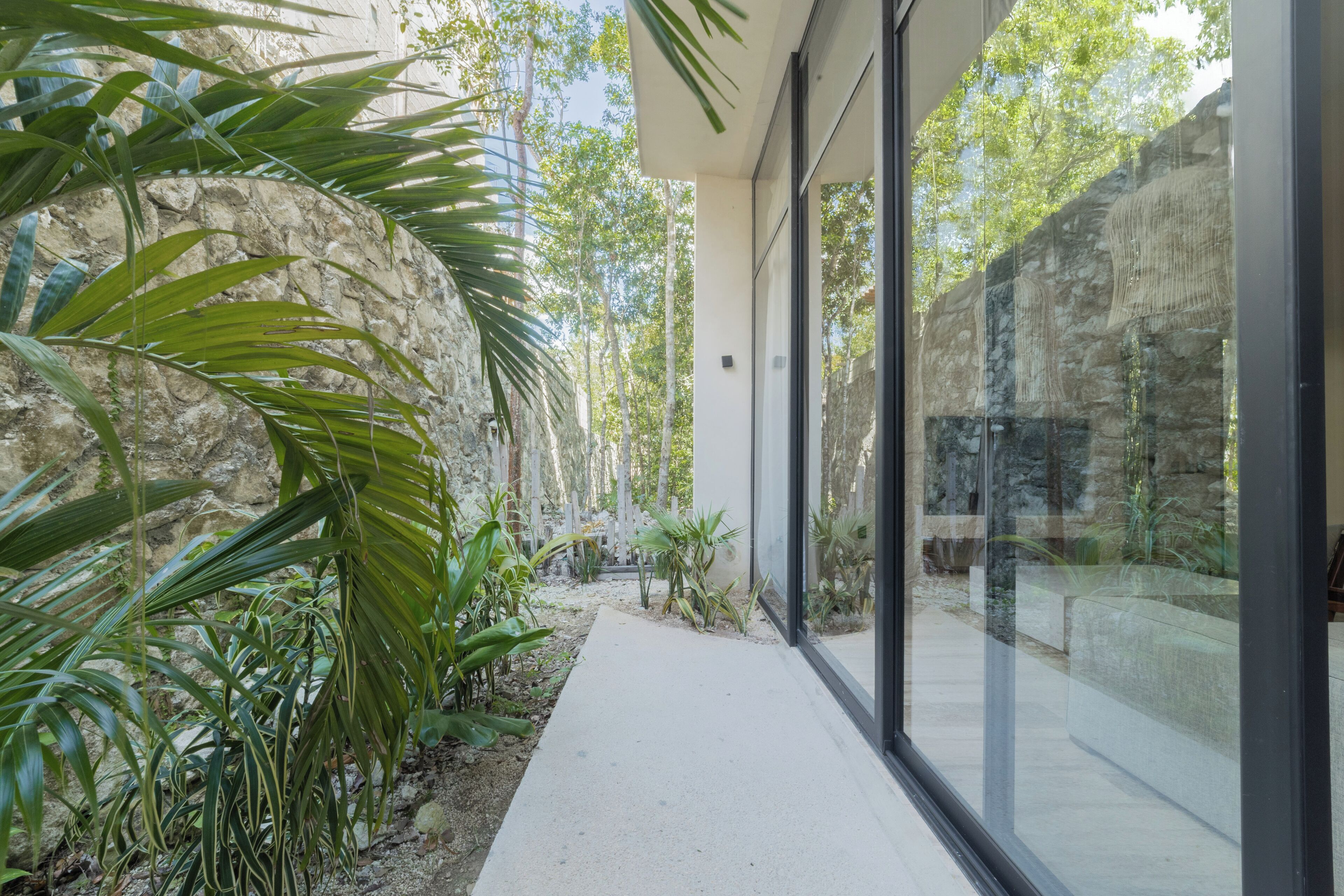 Un edificio moderno con amplios ventanales de vidrio, una pared de piedra y abundante vegetación.