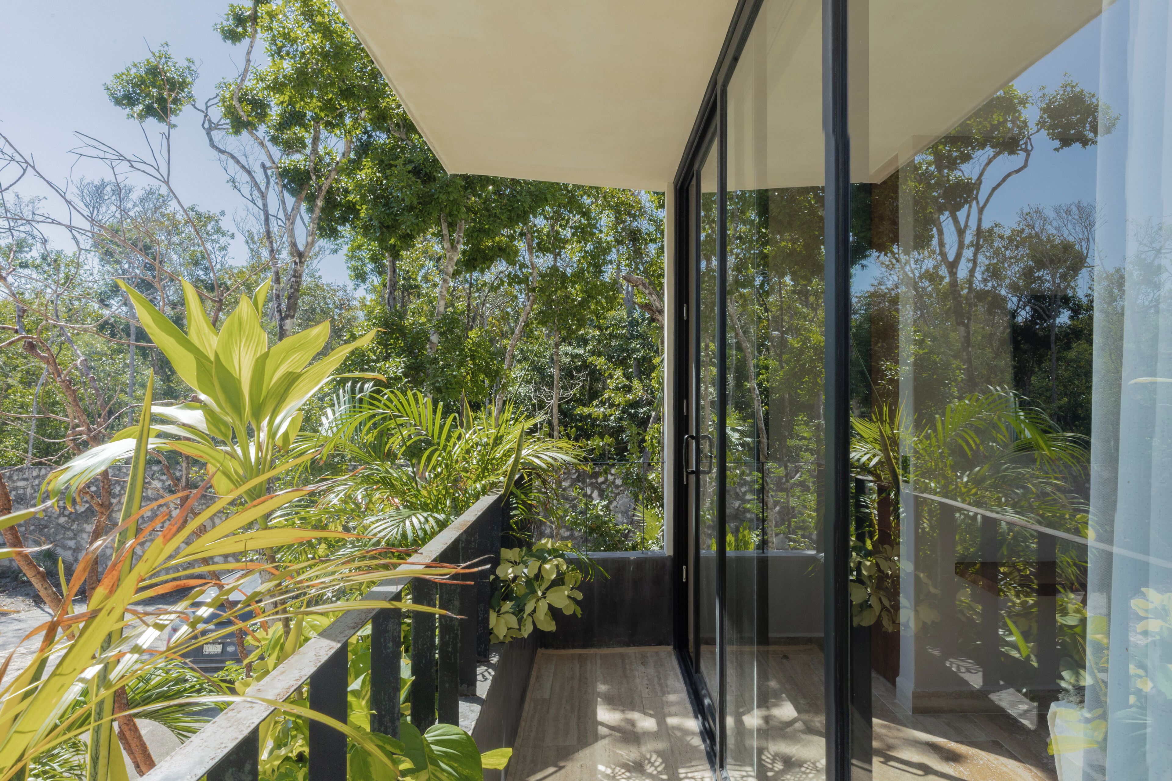 A modern balcony with glass doors, surrounded by lush greenery and trees.