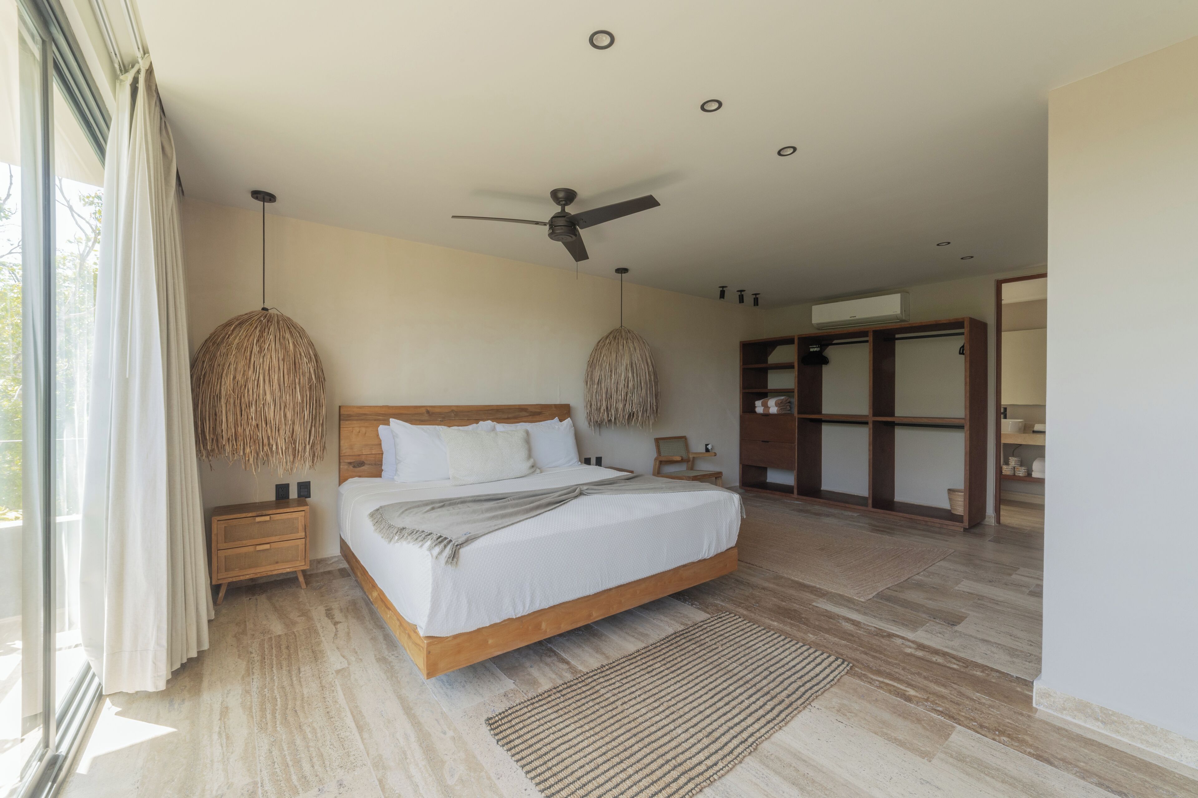 A bedroom with a large bed, wooden headboard, two bedside tables, a ceiling fan, and a wardrobe.