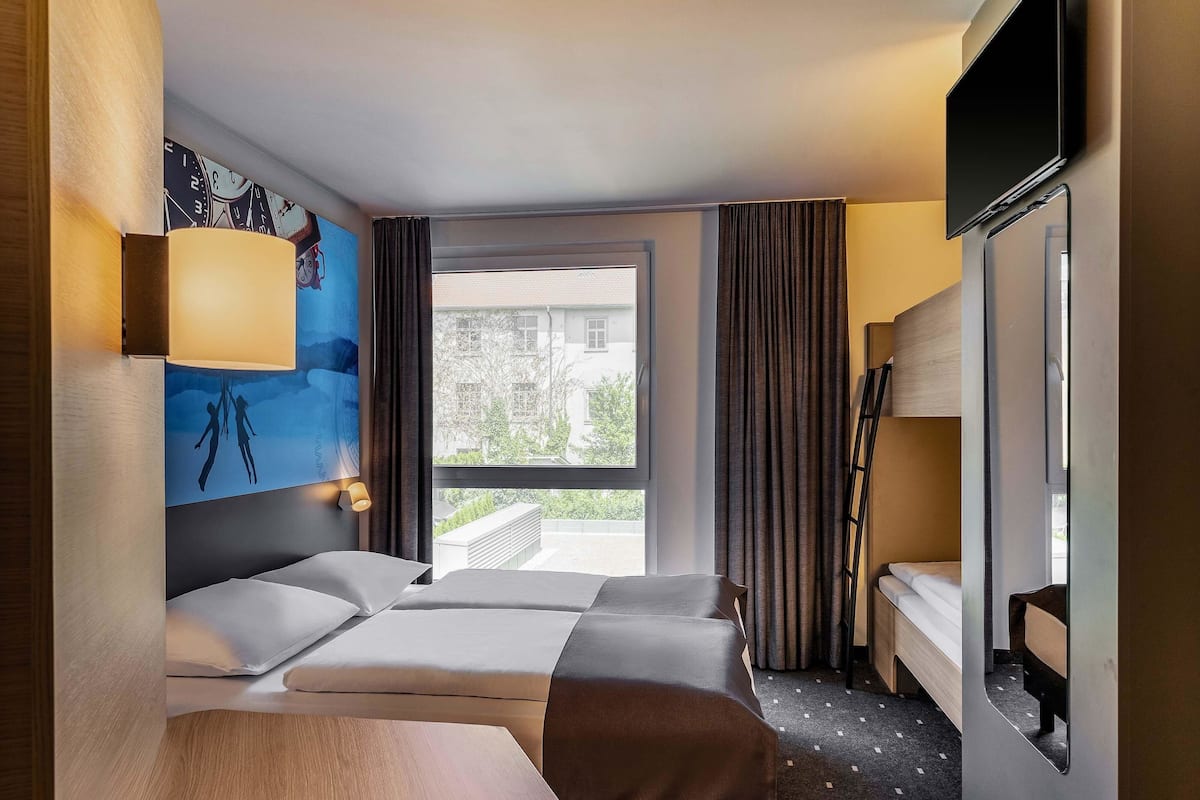 Habitación de hotel con dos camas, un ventanal grande, un cuadro en la pared y un televisor montado.