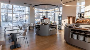 Una cafetería moderna con mostrador central, zona de estar y grandes ventanales.