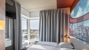 Una habitación de hotel moderna con una cama grande, un escritorio y vistas a la ciudad a través de la ventana.