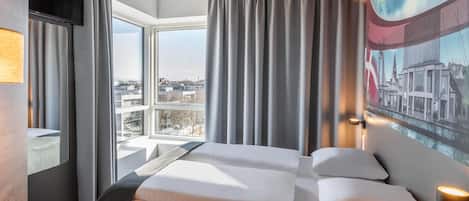 Una habitación de hotel moderna con una cama grande, un escritorio y vistas a la ciudad a través de la ventana.