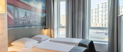 A hotel room with two beds, a desk, a painting of a cityscape, and a view of buildings and cars through the window.