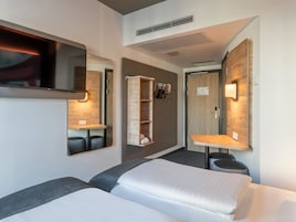 Una habitación de hotel moderna con dos camas, televisor, armario empotrado y espejo.