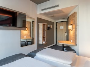 Quarto de hotel moderno com duas camas, televisão, guarda-roupa embutido e espelho.
