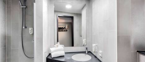 A modern bathroom with grey tiles, a black countertop sink, a handheld showerhead, and a towel rack.