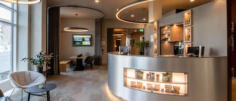 Una moderna area di reception con una scrivania a forma di curva, uno schermo digitale e una macchina per il caffè.