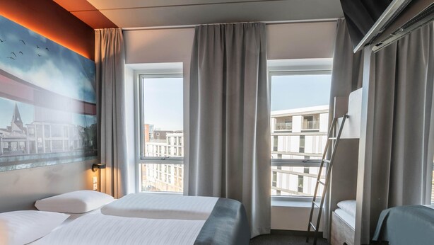 Habitación de hotel con dos camas, un ventanal con cortinas, un cuadro en la pared y vistas a edificios.