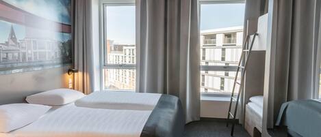 A hotel room with two beds, a large window with curtains, a painting on the wall, and a view of buildings outside.