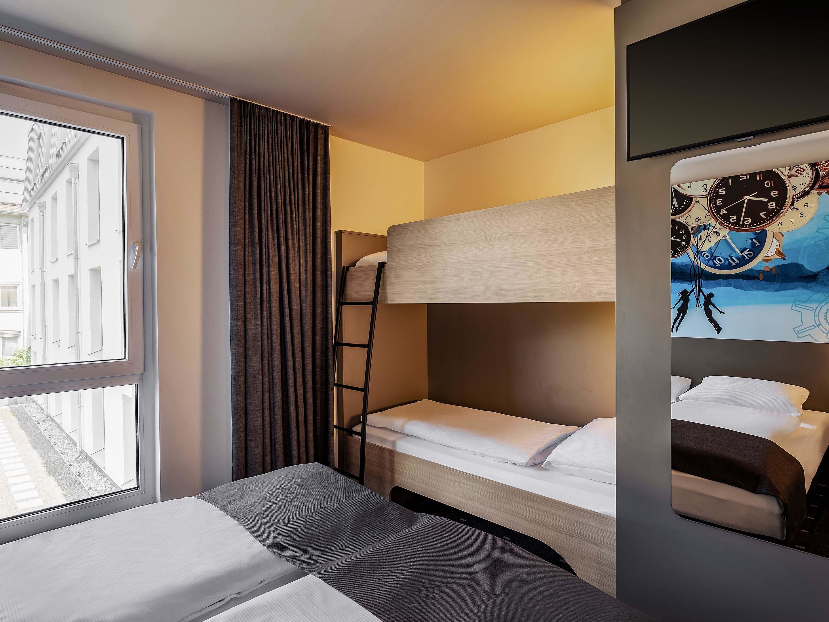 Une chambre d’hôtel avec un lit superposé, une fenêtre avec des rideaux, une horloge murale et un tableau.
