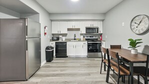 A compact kitchen with white cabinets, stainless steel appliances, and a wooden dining table.