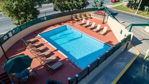 Ein Pool auf dem Dach mit Liegestühlen und Sonnenschirmen, umgeben von einem grünen Zaun.