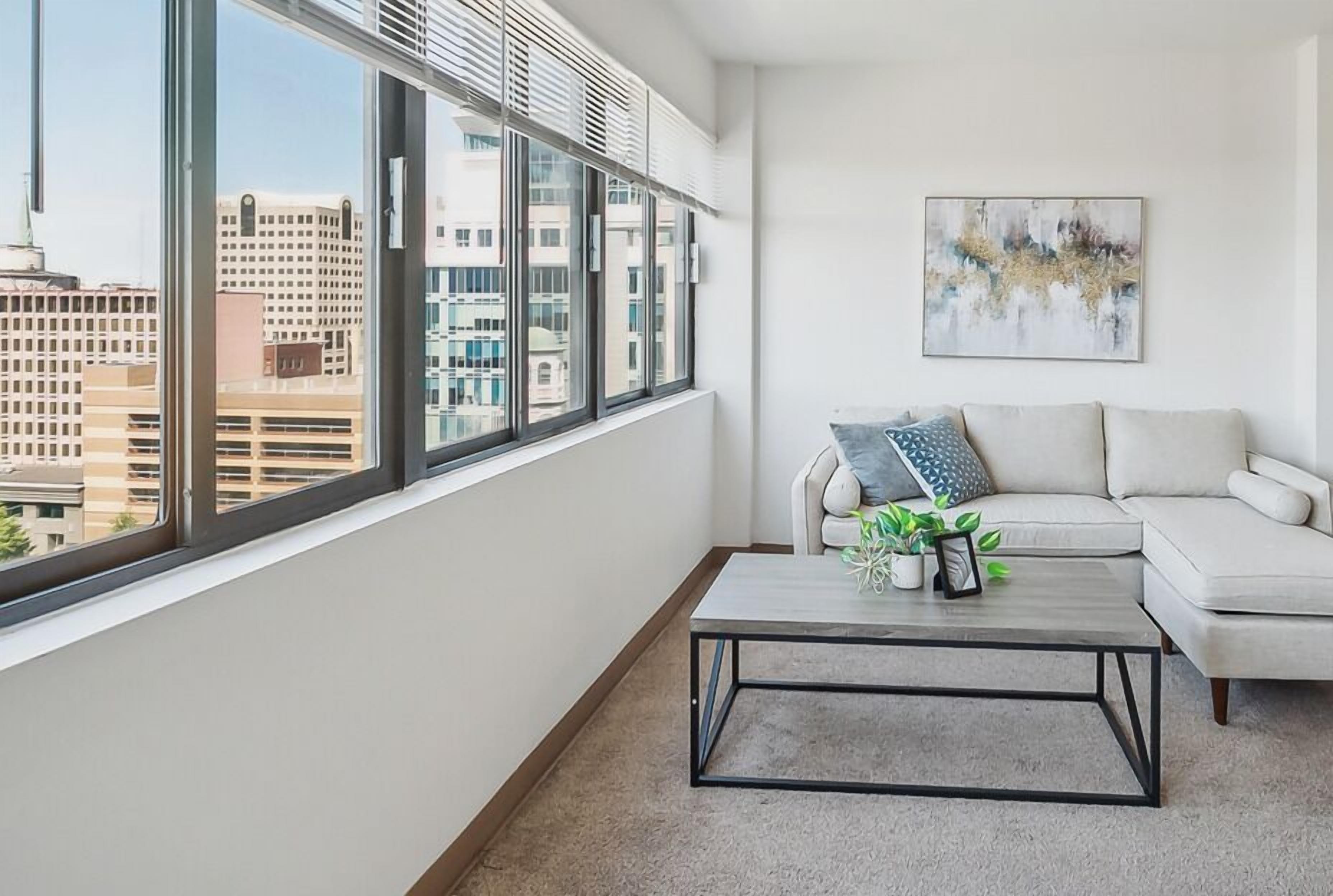 A modern living room with a large window, a white sofa, a coffee table, and a city view.