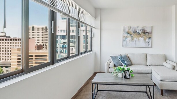 Ein modernes Wohnzimmer mit großem Fenster, einem weißen Sofa, einem Couchtisch und Blick auf die Stadt.