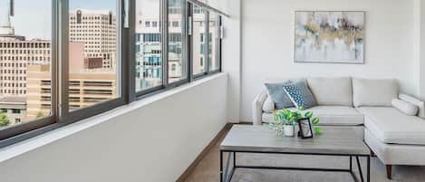 A modern living room with a large window, a white sofa, a coffee table, and a city view.