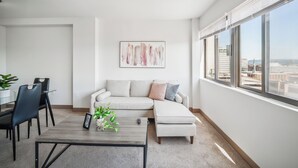 A modern living room with a sofa, coffee table, and chairs. There is a large window with a city view.