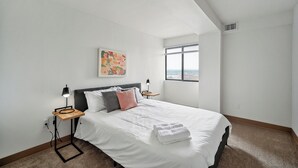 Une chambre à coucher avec un grand lit, une table de chevet, une lampe, un tableau et une fenêtre donnant sur un beau paysage.