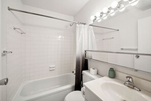 A bathroom with a bathtub, toilet, sink, and a mirror with lights.