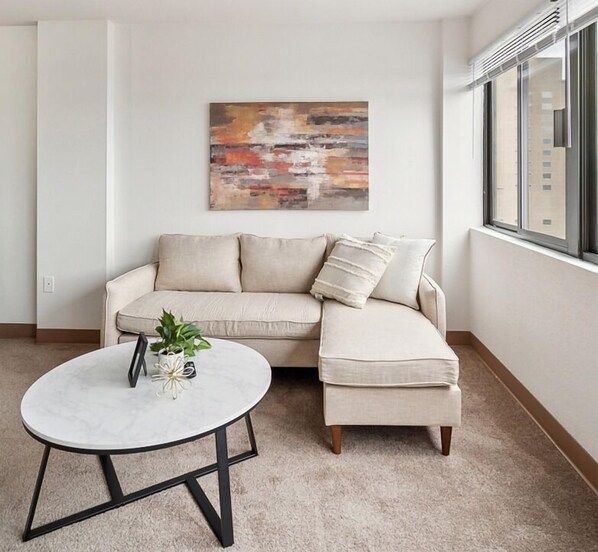 A living room with a beige sectional sofa, a round coffee table, and a painting on the wall.