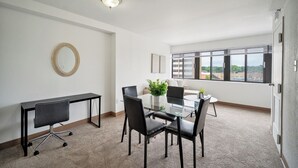 A modern office space with a glass table, black chairs, a round mirror, and a view of the city through large windows.