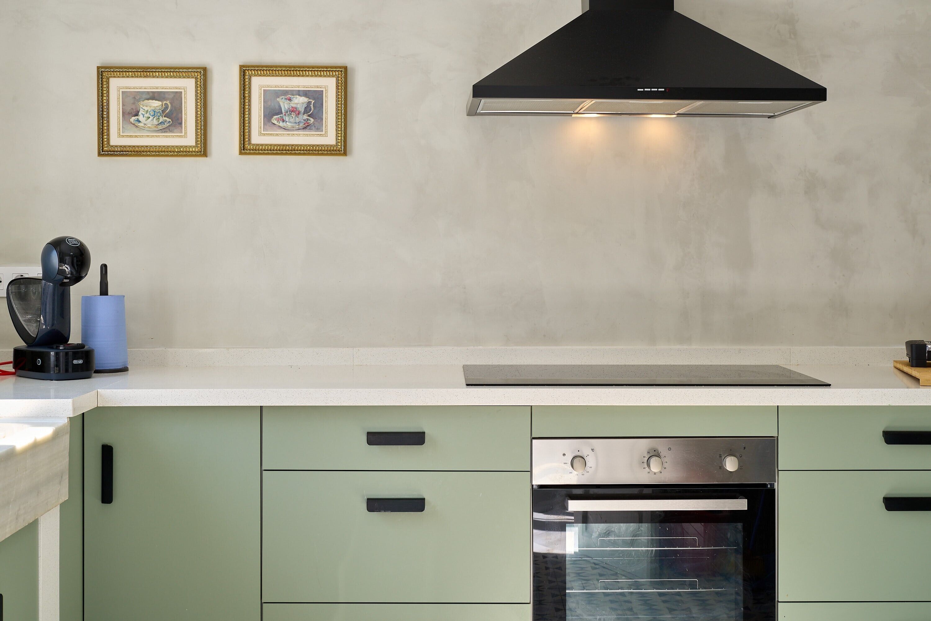 A kitchen with a built-in oven, a black range hood, and two framed pictures on the wall.