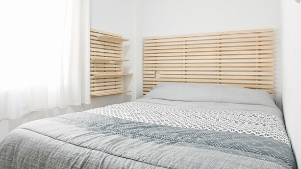 Un dormitorio con cama, cabecera de listones de madera y edredón estampado.