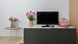 Un televisor sobre un mueble bajo, una mesita redonda con un florero y una furgoneta de juguete en el mueble.
