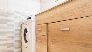 Un lavadero moderno con lavadora de carga frontal, armarios de madera y paredes con azulejos.
