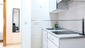 A modern kitchen with white cabinets, a stainless steel sink, and a black faucet. There is a mirror on the wall and a window above the sink. - Cozy Apartment in Vallecas (Madrid)