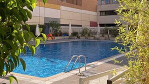A swimming pool with a metal ladder, surrounded by a tiled deck and some greenery. - Modern Family Apartment with Terrace and Pool in Madrid Tempory (Madrid)
