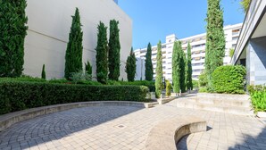 A paved courtyard with a curved pathway, surrounded by neatly trimmed hedges and tall cypress trees. - Modern Family Apartment with Terrace and Pool in Madrid Tempory (Madrid)
