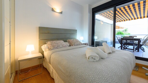 A modern hotel room with a large bed, a bedside table with a lamp, and a view of the outdoor patio. - Modern Family Apartment with Terrace and Pool in Madrid Tempory (Madrid)