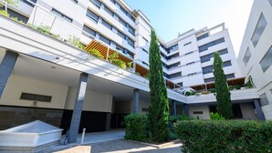 A modern building with multiple floors, balconies with plants, and a central courtyard with a seating area and a small pool. - Modern Family Apartment with Terrace and Pool in Madrid Tempory (Madrid)