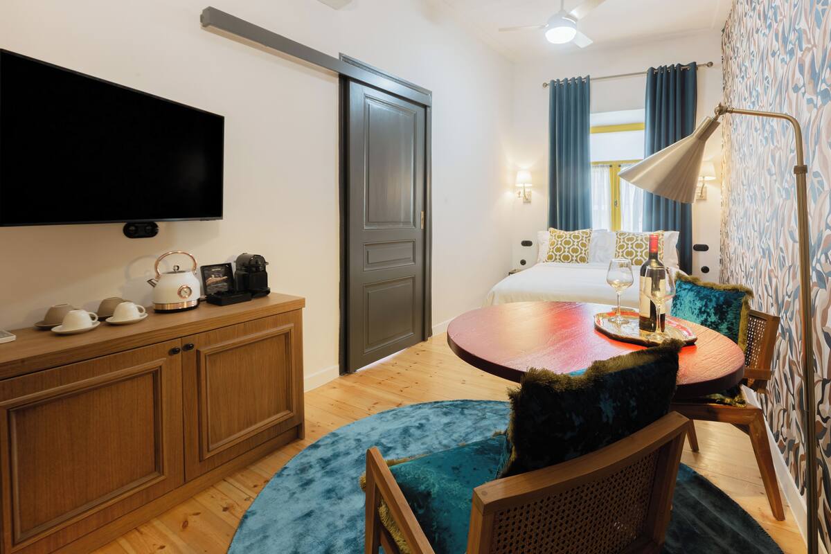 A hotel room with a TV, wooden furniture, a round table with a blue rug, and a bed with blue curtains.