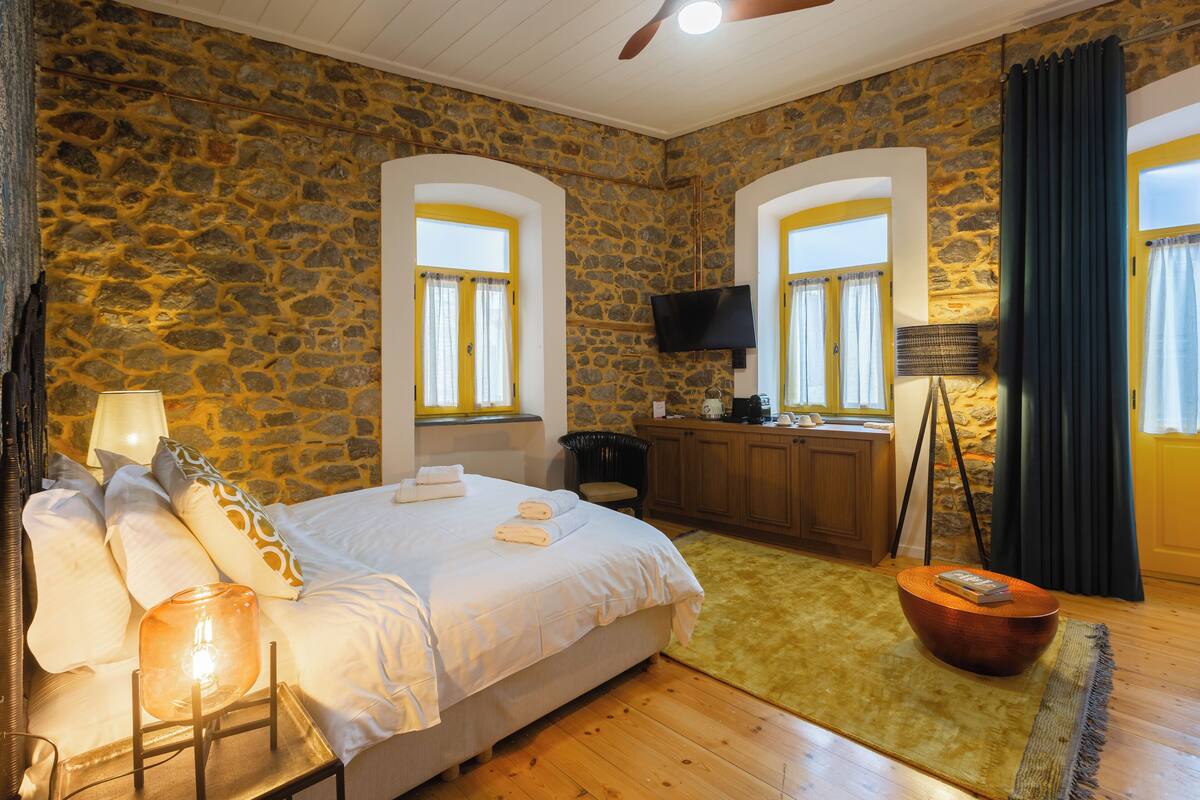 A bedroom with a stone wall, a bed with white linens, a flat-screen TV, and a wooden floor.