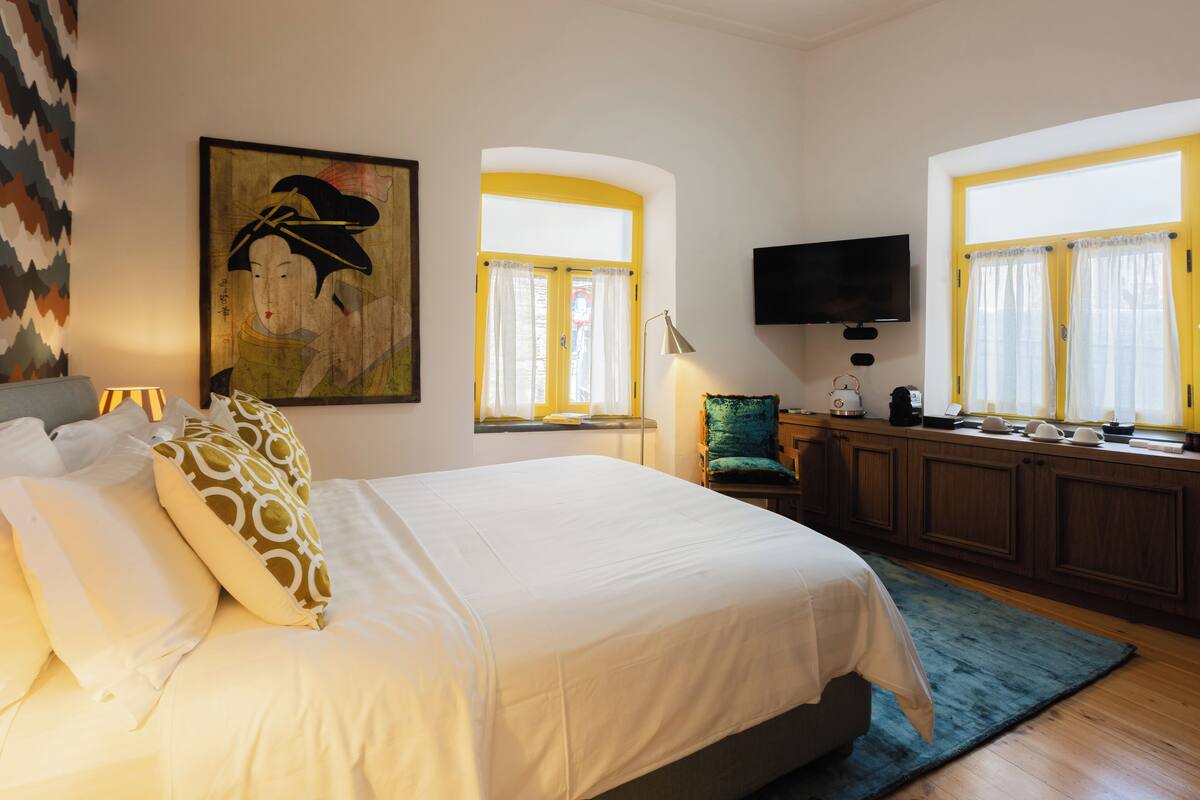 A hotel room with a large bed, a television, a desk, and a window with curtains.
