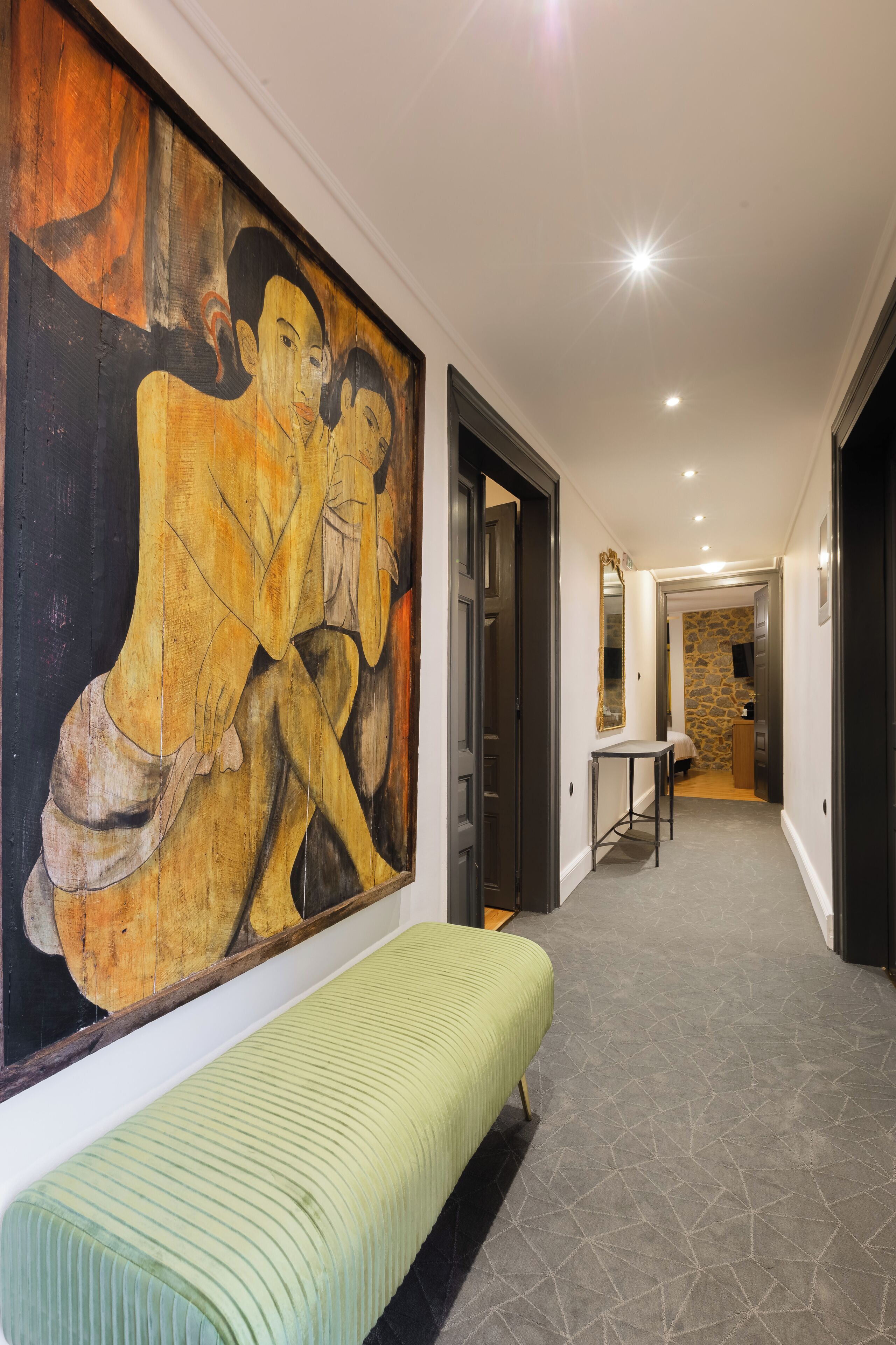 Un couloir orné d’un grand tableau abstrait, avec un banc et un mur de pierre en arrière-plan.
