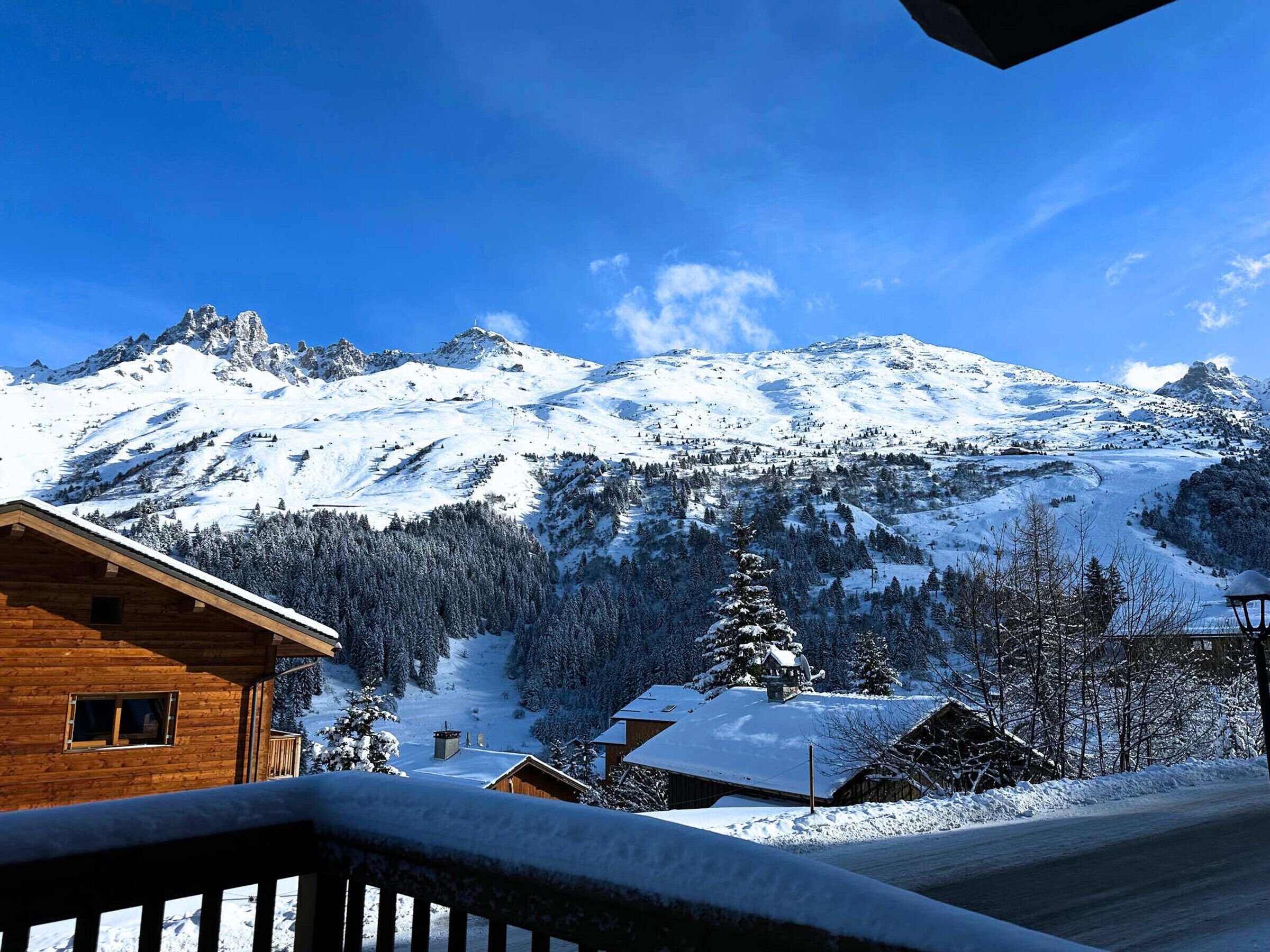 Una baita di legno con tetto innevato, immersa in un paesaggio montuoso sotto un cielo azzurro terso.