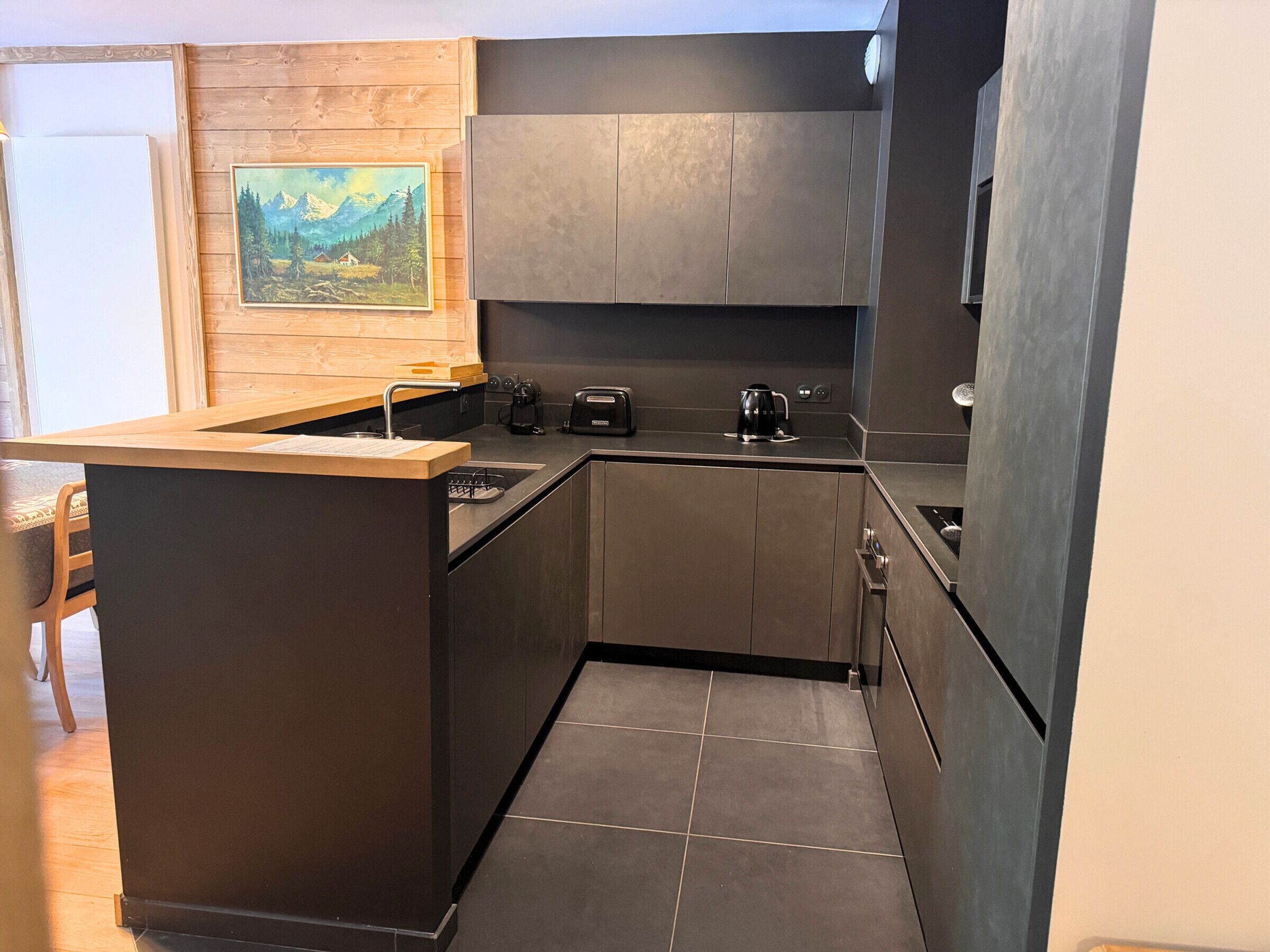 Eine moderne Küche mit dunklen Schränken, einer Holz Arbeitsplatte und einem Gemälde an der Wand.