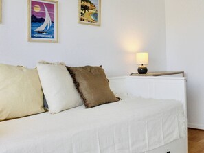 A white sofa with three pillows, a lamp on a bedside table, and two framed pictures on the wall.