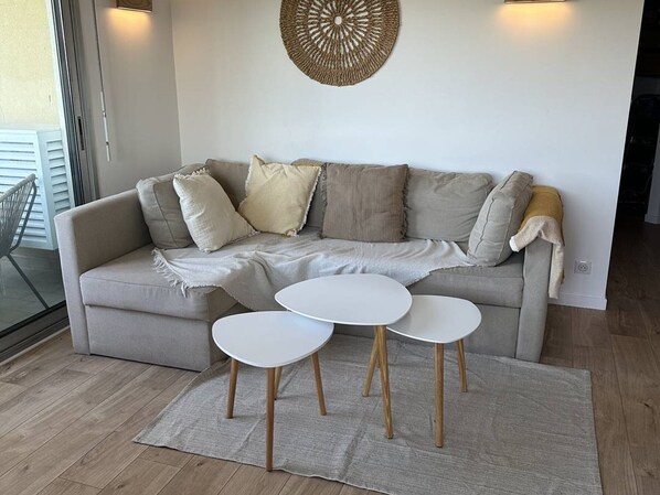 A living room with a beige sofa, two white round tables, and a woven wall decoration.