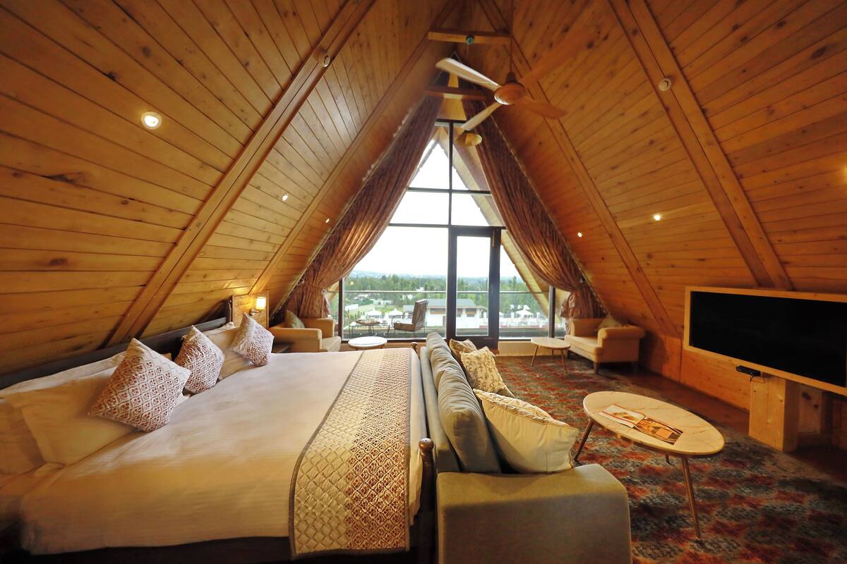 A cozy bedroom with a large bed, a sofa, a TV, and a view of the outdoors.