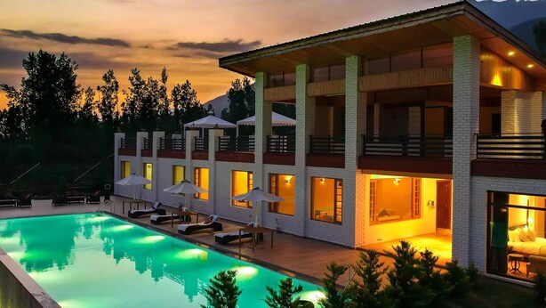 A modern hotel with a swimming pool, multiple balconies, and a view of the mountains. - Rah Bagh (Srinagar)