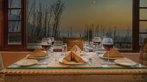 A dining table set for two with wine glasses, plates, and napkins, overlooking a scenic landscape. - Rah Bagh (Srinagar)