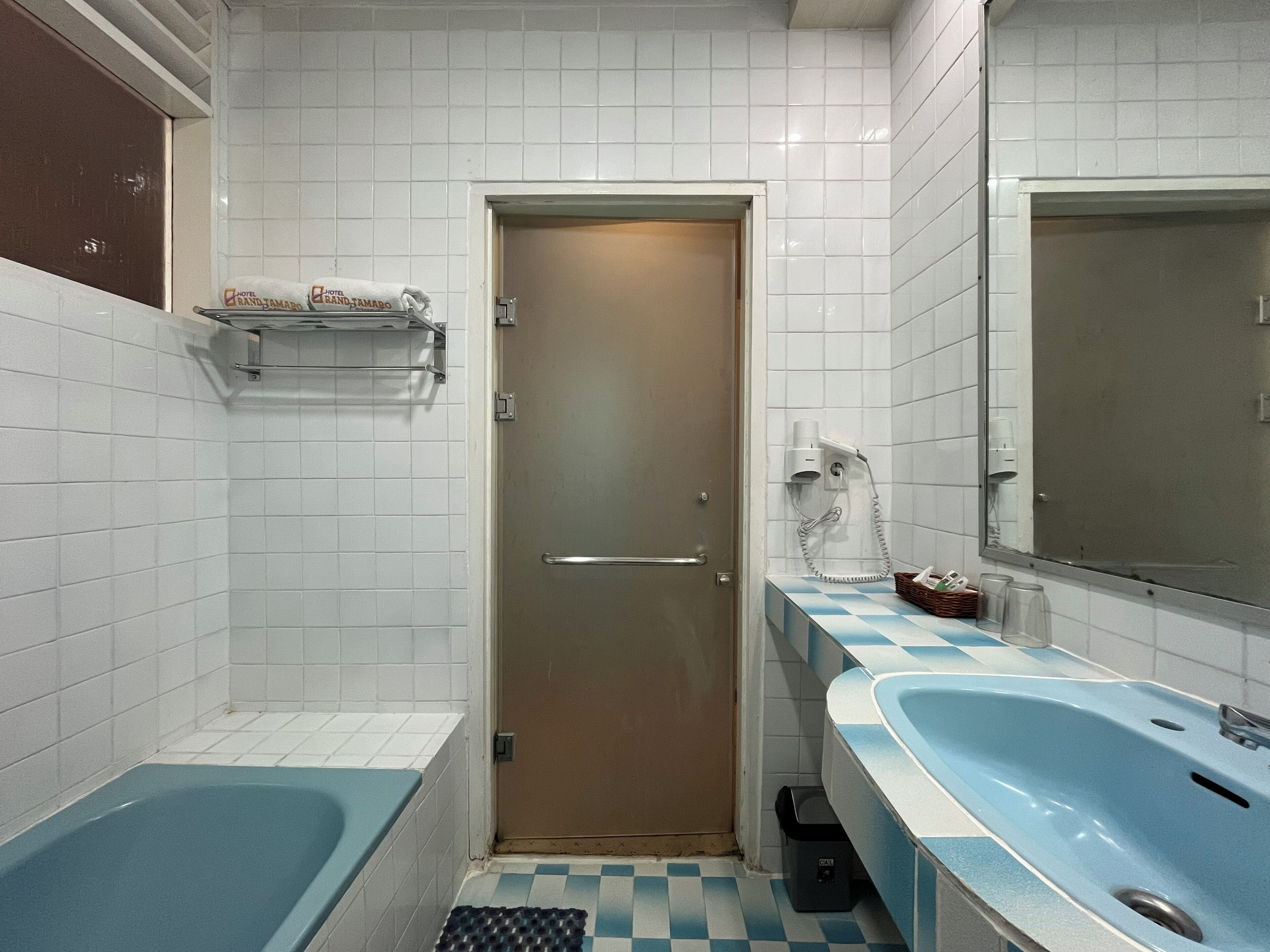 Un baño con bañera, lavamanos, espejo, toallero y una puerta.